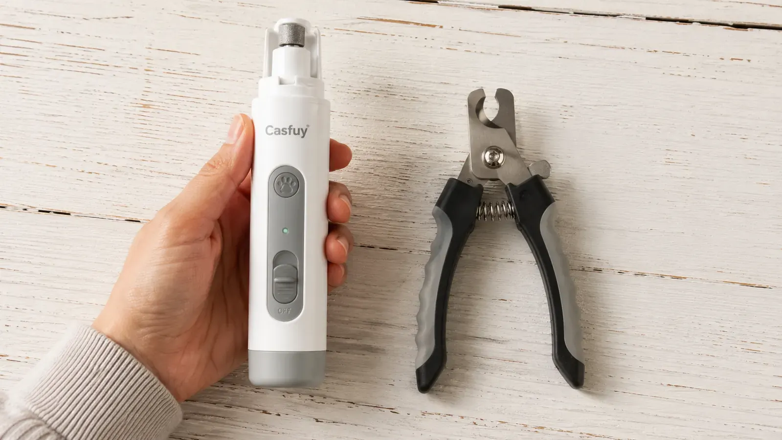 Casfuy electric nail grinder in hand next to a pair of traditional dog nail clippers on a white surface
